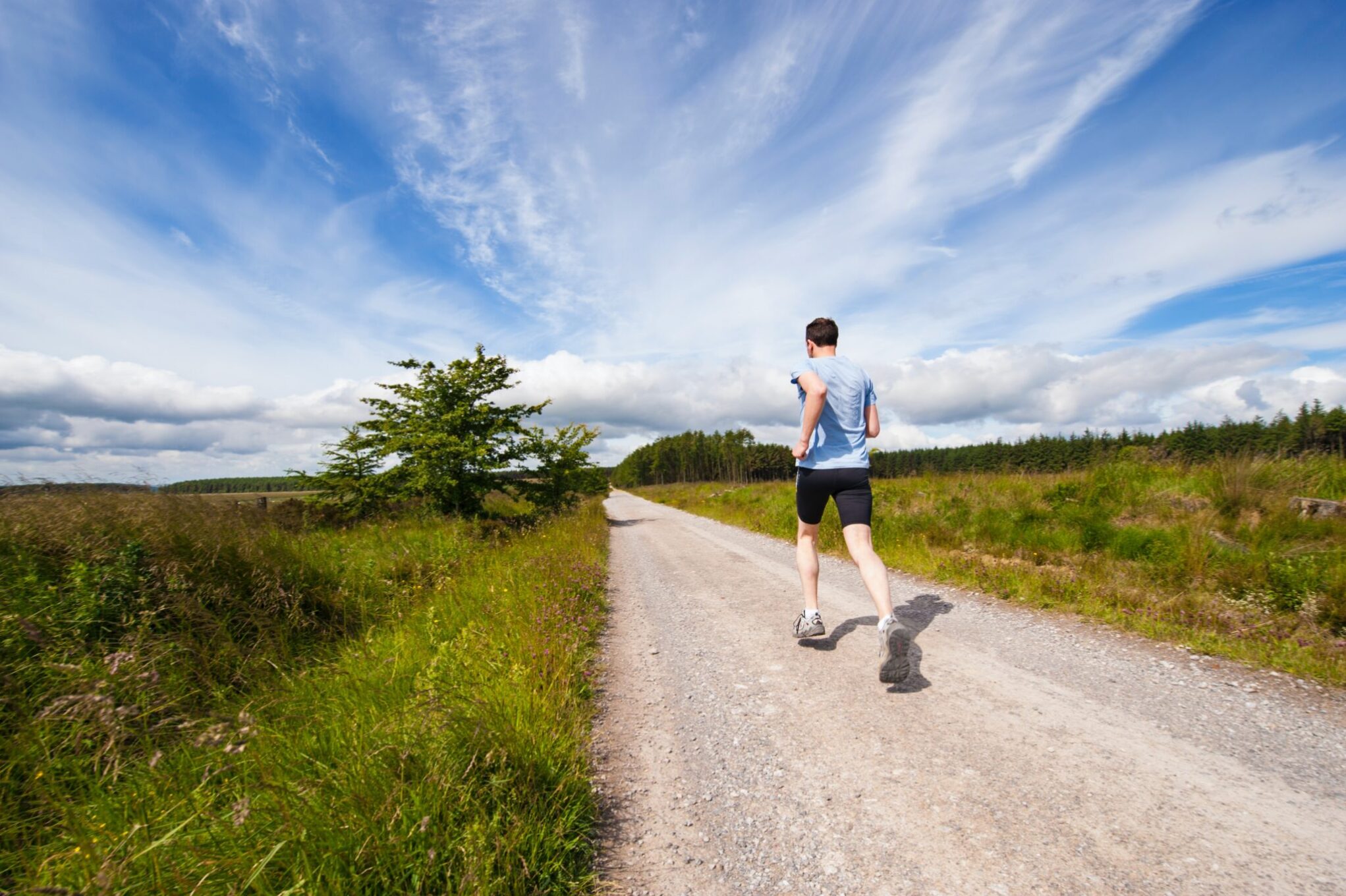 Man runs on dirt road out for a jog under bright blue sky